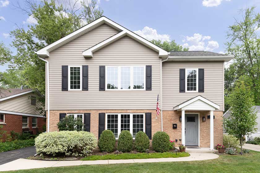 A two story suburban home with brick and tan vinyl siding