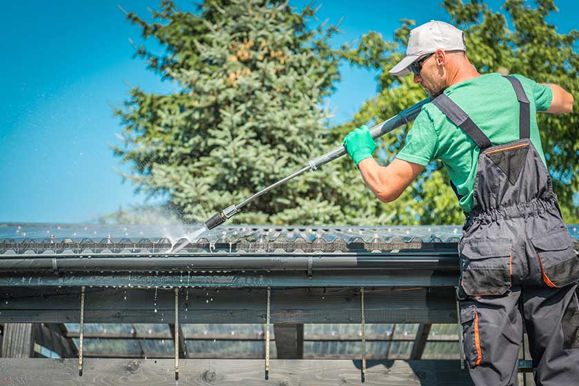 Roof and Gutters Power Cleaning Using Pressure Washer. Caucasian Worker